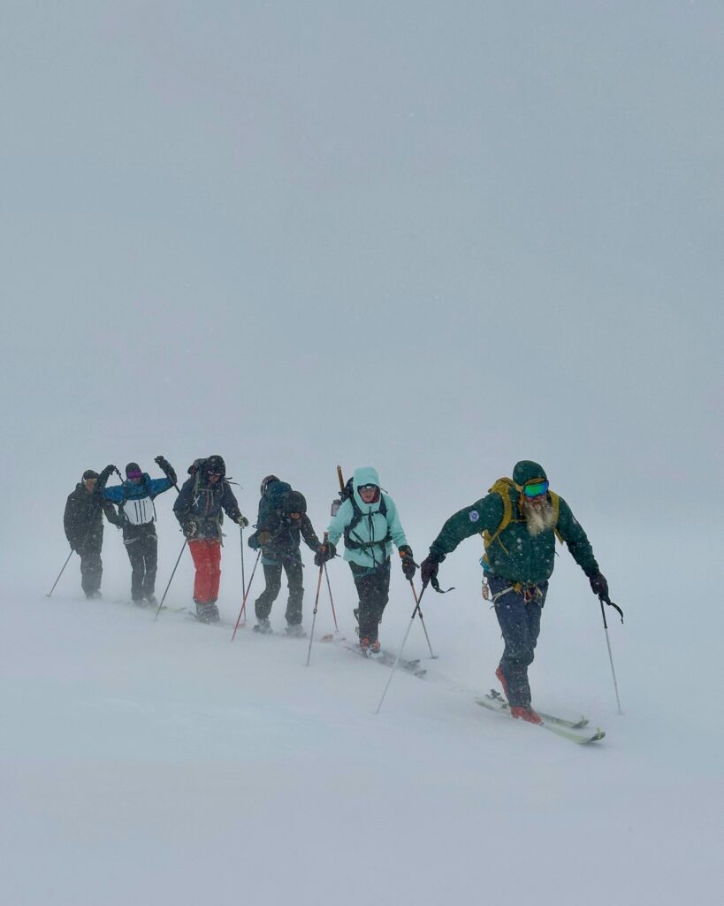 A group of skiers traversing a snowy landscape in challenging winter weather conditions.